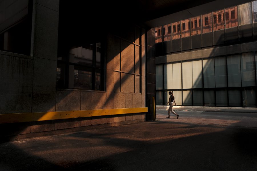 A person walks across a downtown alley as light is reflected onto the street from a nearby building.