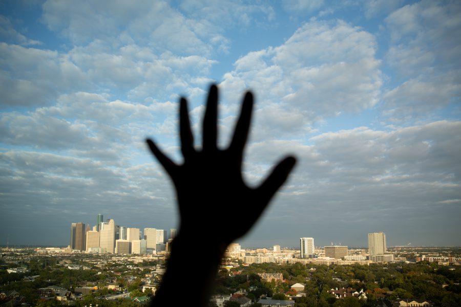 A hand is silhouetted reaching out against a window with a downtown skyline seen beyond.