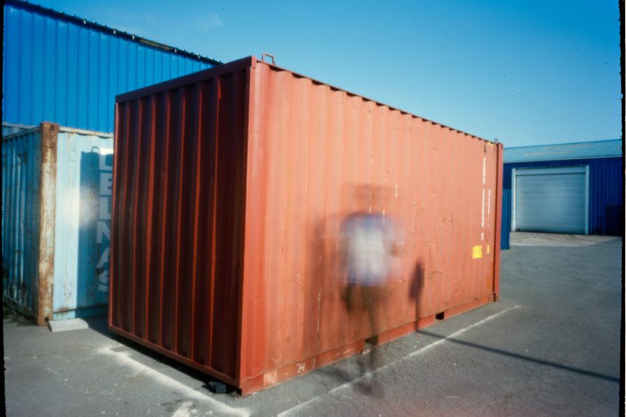 This is an out of focus refugee photographed in front of a red container.