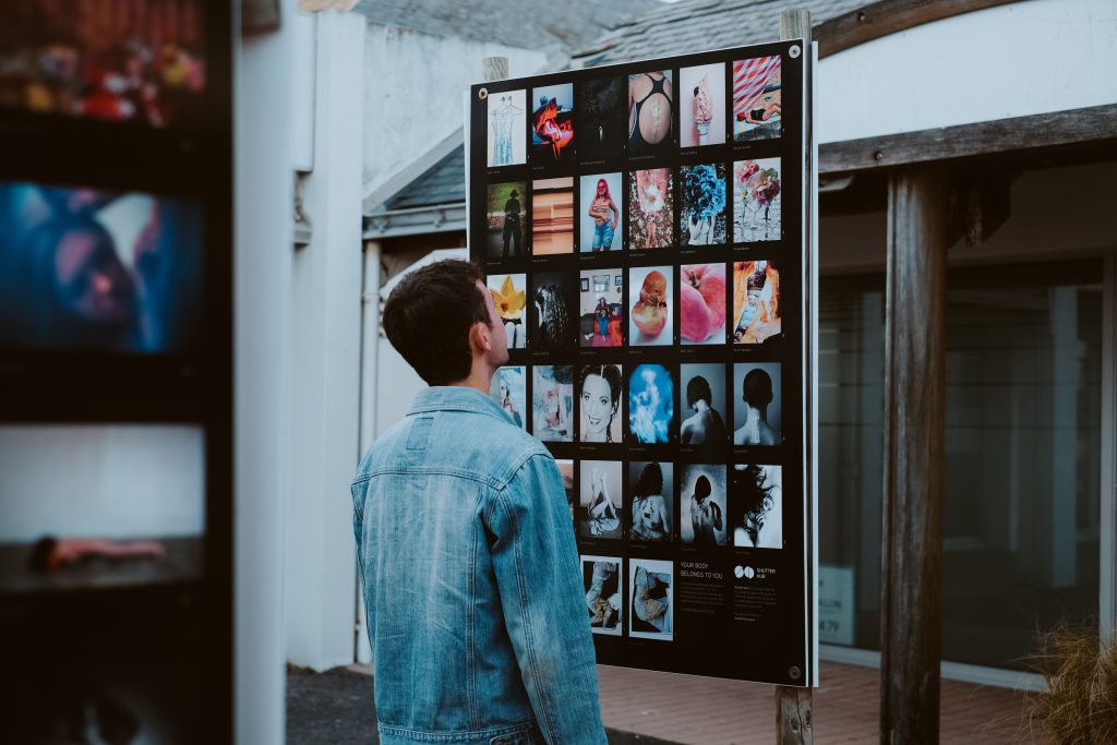 a man in a denim blazer looks at a poster board of exhibition images in an outdoor space