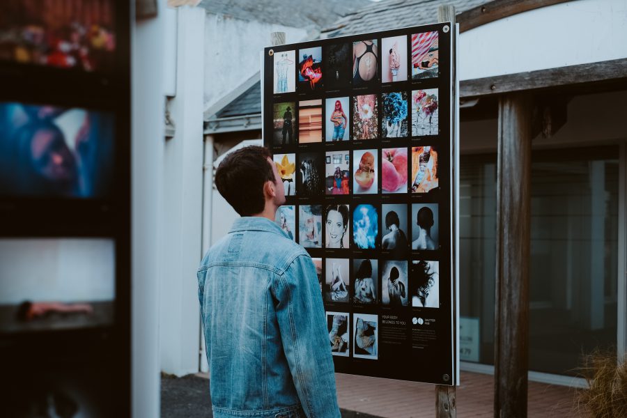 a man in a denim blazer looks at a poster board of exhibition images in an outdoor space