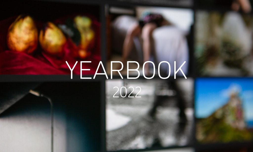 Graphic with 'YEARBOOK 2022' in white in the centre, and an out of focus photograph of a monitor showing the YEARBOOK 2021 online exhibition behind