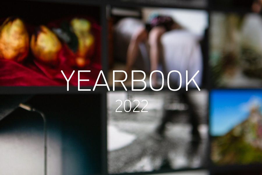 Graphic with 'YEARBOOK 2022' in white in the centre, and an out of focus photograph of a monitor showing the YEARBOOK 2021 online exhibition behind