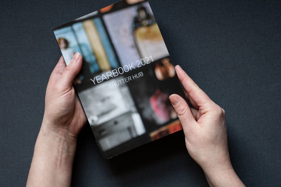 Photograph of hands holding a copy of the YEARBOOK printed publication, with the text 'YEARBOOK 2021', Shutter Hub' on the cover, against a dark grey fabric background