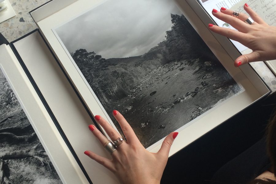 Hands with red painted nails and ornate rings either side of a box with a black and white photograph