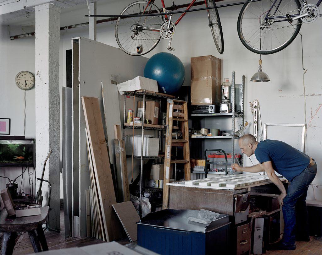 A man makes soaps with street-found objects enclosed in glycerin in his open-space living room repurposed as a workshop.