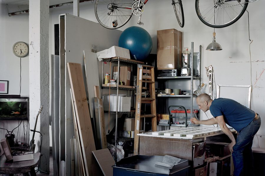 A man makes soaps with street-found objects enclosed in glycerin in his open-space living room repurposed as a workshop.