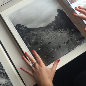 Hands with red painted nails and ornate rings either side of a box with a black and white photograph