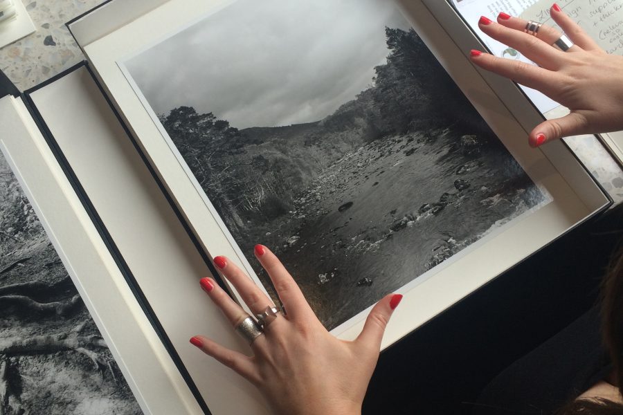 Hands with red painted nails and ornate rings either side of a box with a black and white photograph